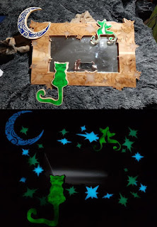 A mirror framed in wood, with glow in the dark resin accents in the shape of a moon, cats, and stars.