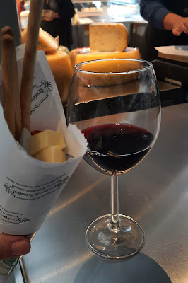 copo de vinho e um cone de papel com vários pedaços de queijos