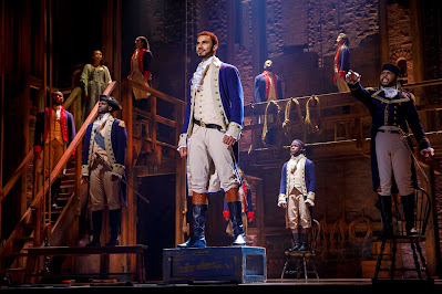 People in colonial costumes are standing on the stage of Hamilton.