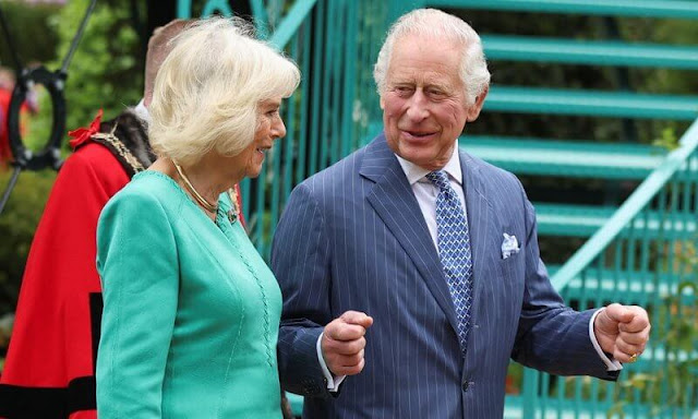 Queen Camilla wore a blue midi dress. The Queen wore an ivory two-tone coat and white midi dress. Coronation Garden in Newtownabbey