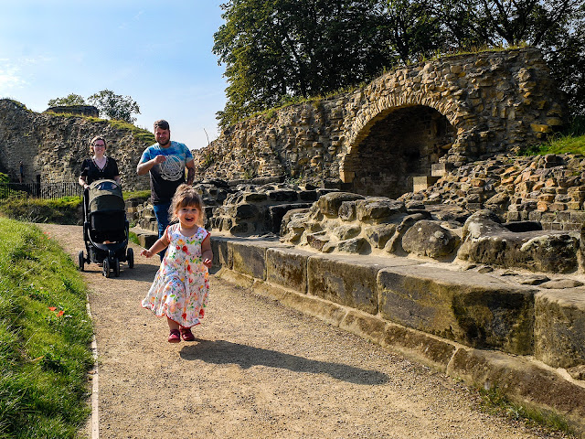 A very young visitor running ahead of their grownups, beaming, in the grounds at Pontefract Castle