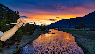 A photo of a sunset being painted by a hand holding an artist's paintbrush, symbolising the creativity of painting the world.