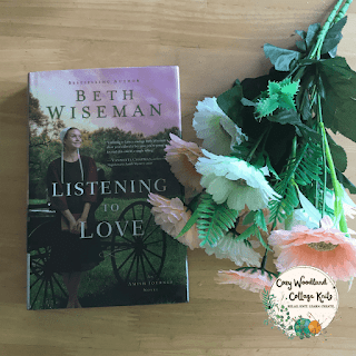 a wooden table with the book listening to love by Beth Wiseman next to a bunch of peach and cream flowers