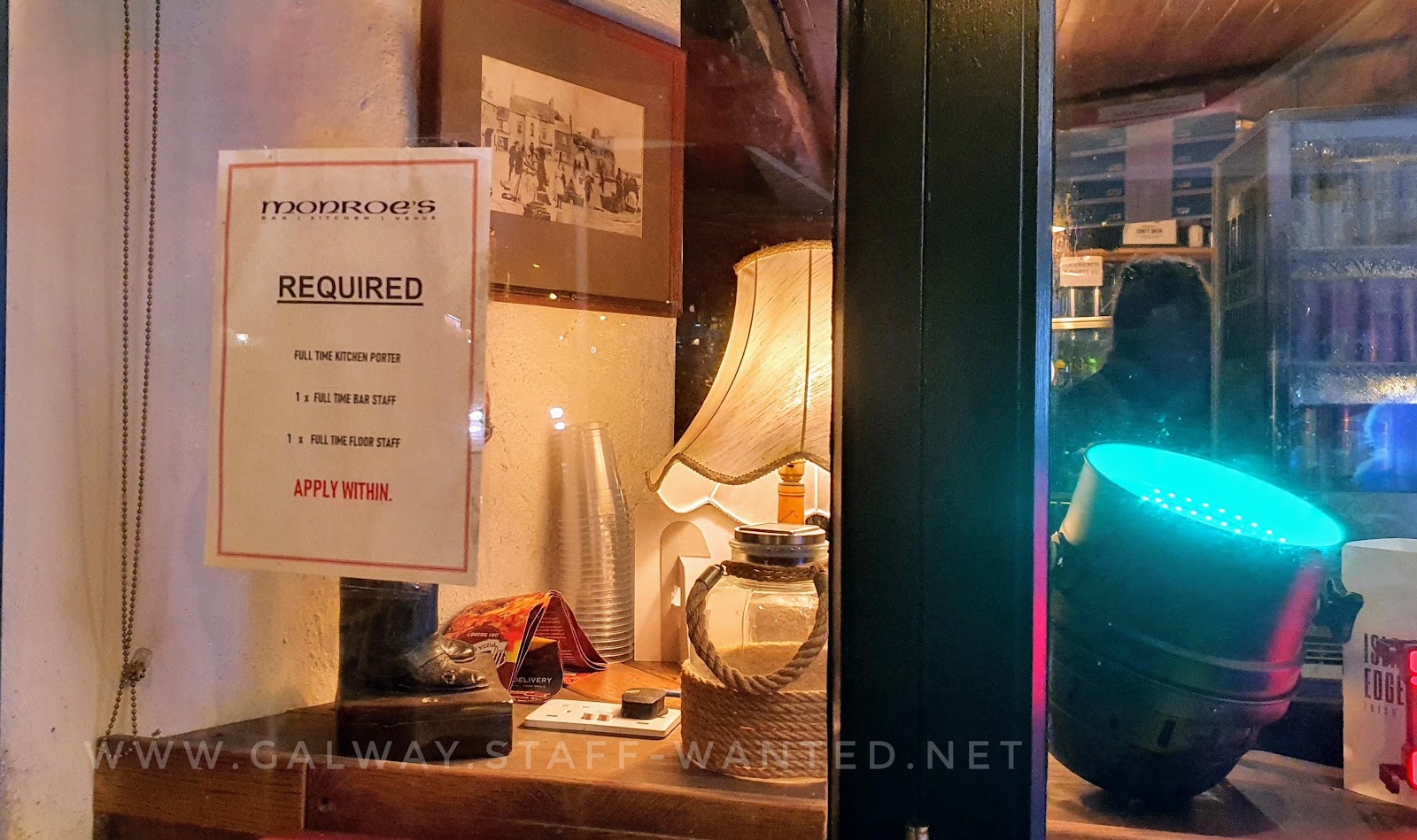 bar window with job advertisement and a large spotlight with a green filter, and an old fashioned table lamp