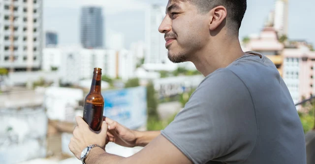 Man Standing on a Balcony and Drinking Beer