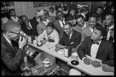 black and white photo of Malcolm X photographing Cassius Clay, in a diner in Miami, 1964