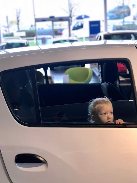 A toddler in the back seat of a car in a car show room