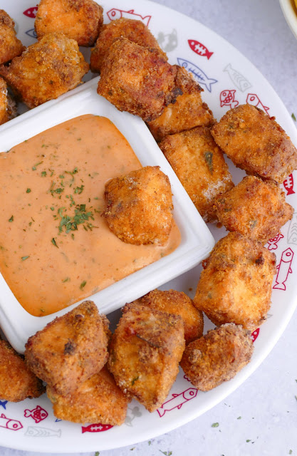 salmon nuggets on a plate with a bowl of dipping sauce in the middle with a salmon nugget in the sauce.