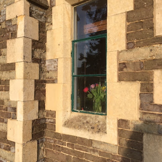 Sunlight streaming onto a stone building with flowers in the window