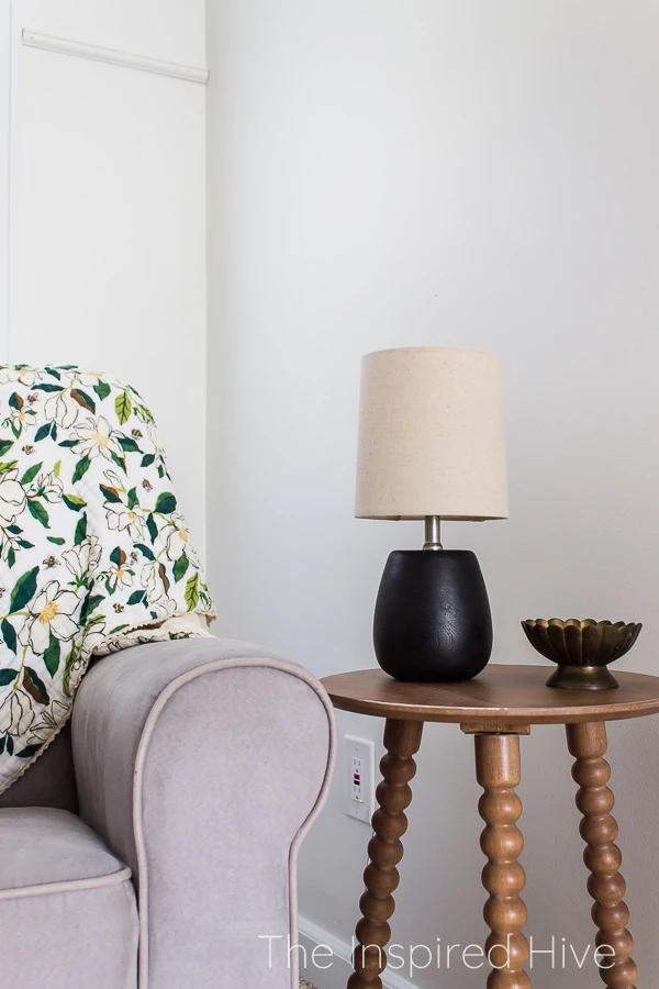 Wooden spindle table with modern traditional lamp next to grey nursery glider