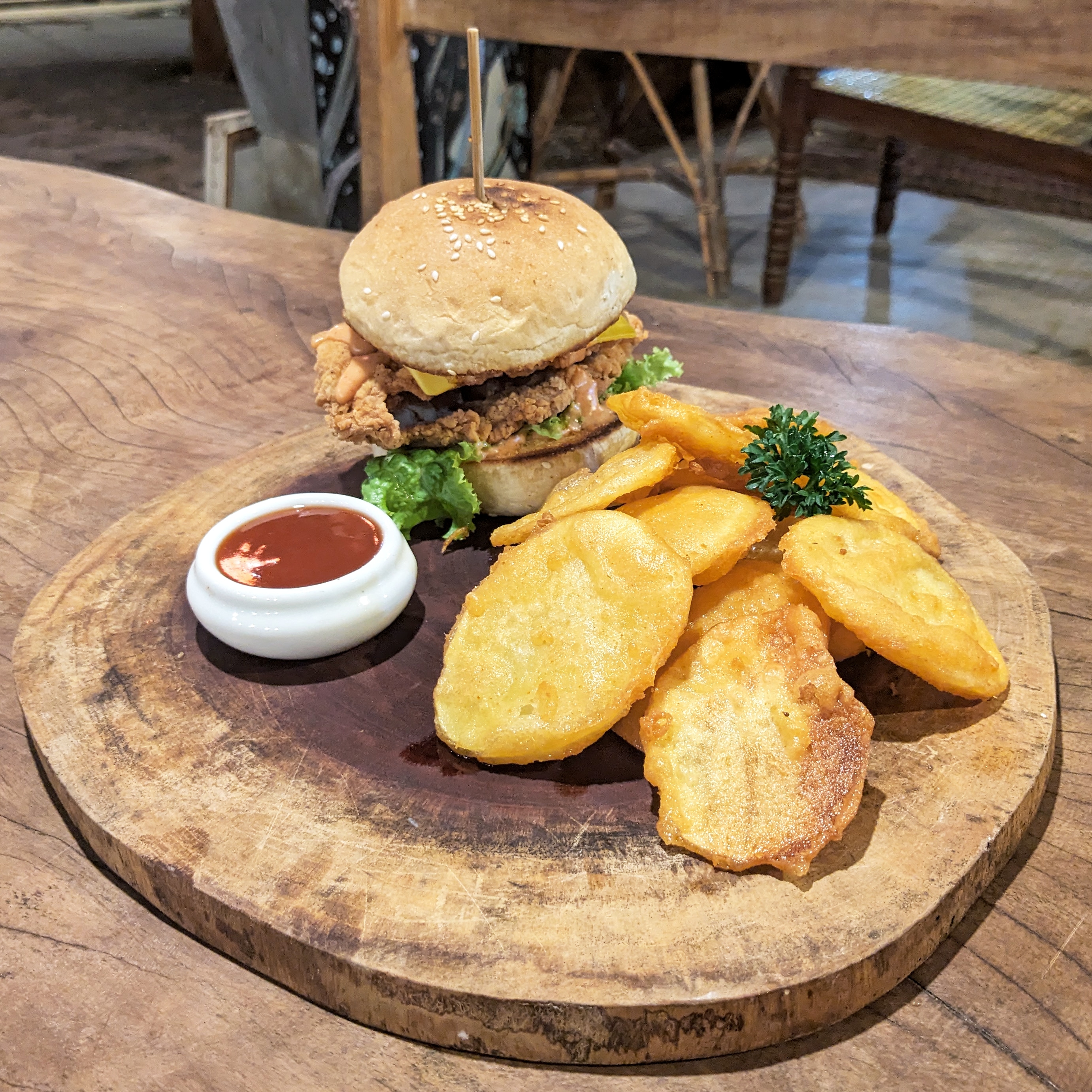 Chicken burger in toasted bun on a wooden serving plate served with potato wedges at Sand Bank, one of the best places to eat in Madiha