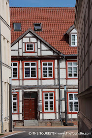 Two storey half– timbered house with a brown entrance door and window frames painted in red.