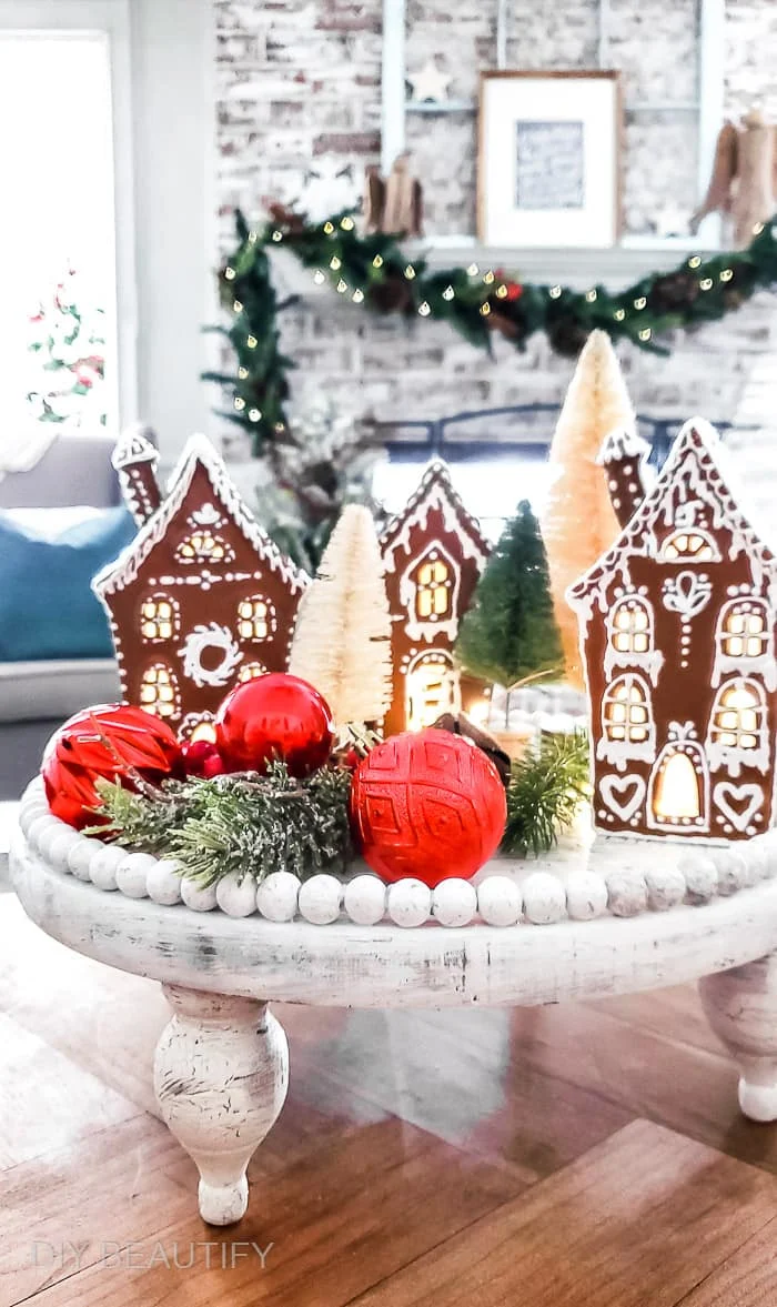 gingerbread cottages styled on white wood tray with ornaments and Christmas greenery