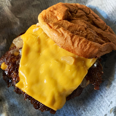 a cheeseburger with the top bun off, showing the melted slice ofcheese