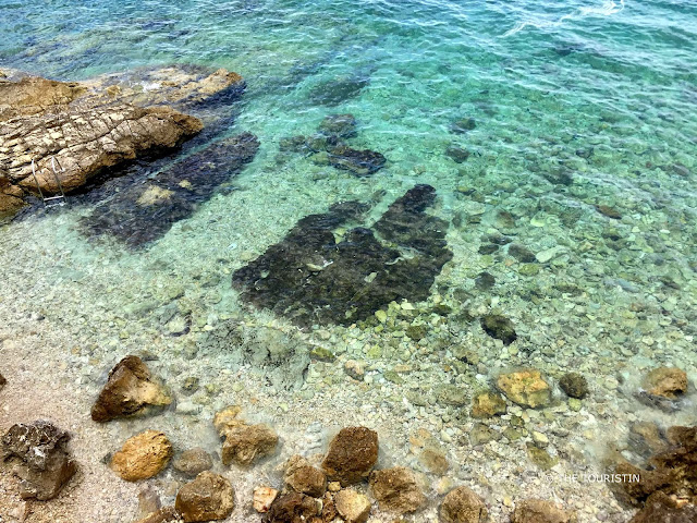 Large boulders and rocks on a beach with crystal clear blue-turquoise water.