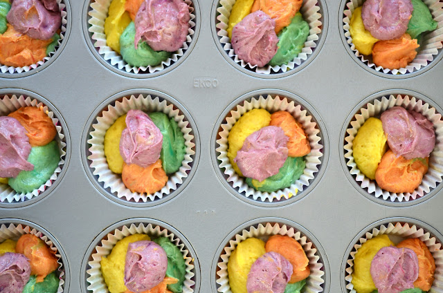 Bunt gefärbter Muffinsteig in Papierförmchen wartet aufs Backen.