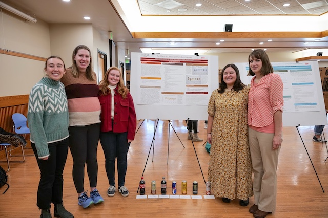 Five female students standing along side a poster they created