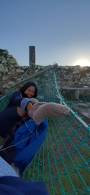 Photograph of a young woman lying in a hammock laughing and raising one foot to show off a newly crocheted sock