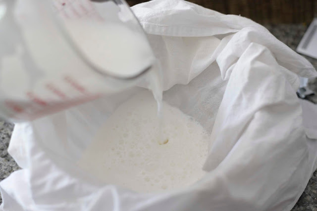 coconut milk being poured into a white flour sack towel over a bowl for straining
