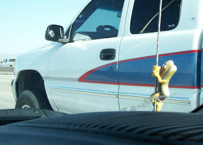 Hot dog antenna topper viewed through windshield with pickup truck in background.