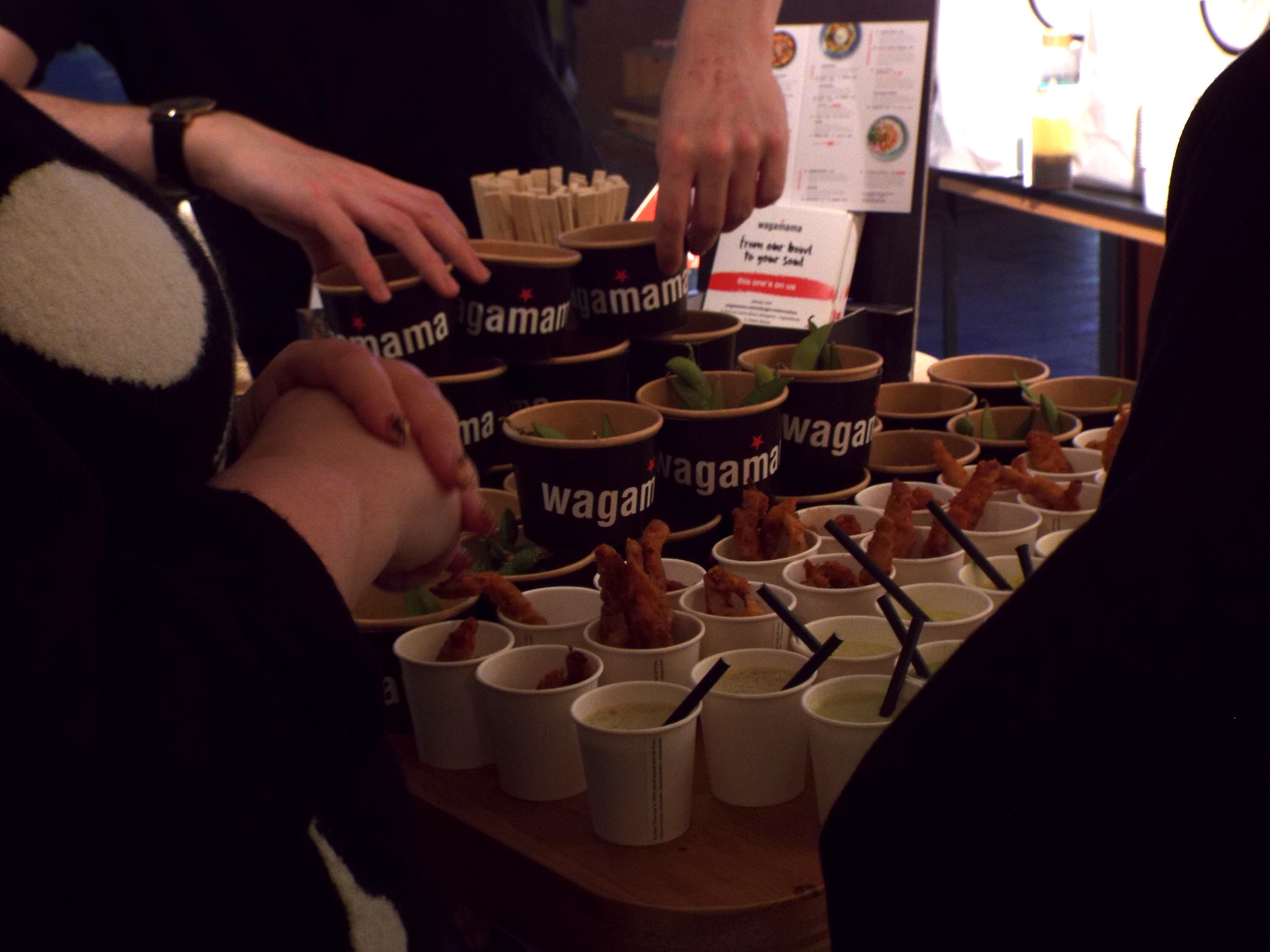 A spread of Wagamama treats in small Wagamama pots and little cups with black paper straws.