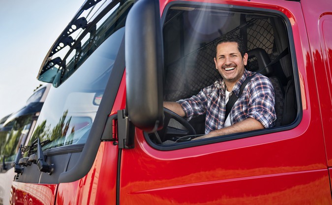 Caminhoneiro sorrindo dentro de um caminhão Volvo FH vermelho