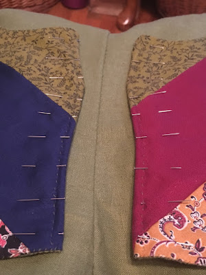 The curved edges of a diagonally-striped patchwork vest, with pins inserted perpendicular to the edges at intervals.