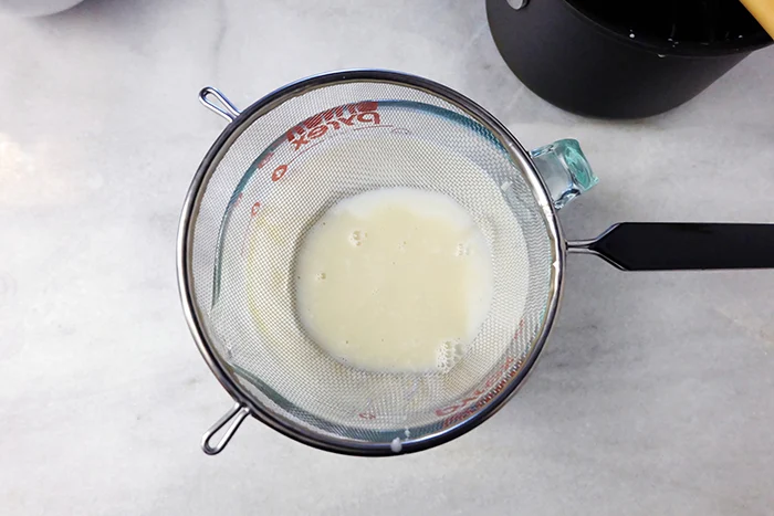 pouring hot cream and gelatin into buttermilk through fine mesh sieve