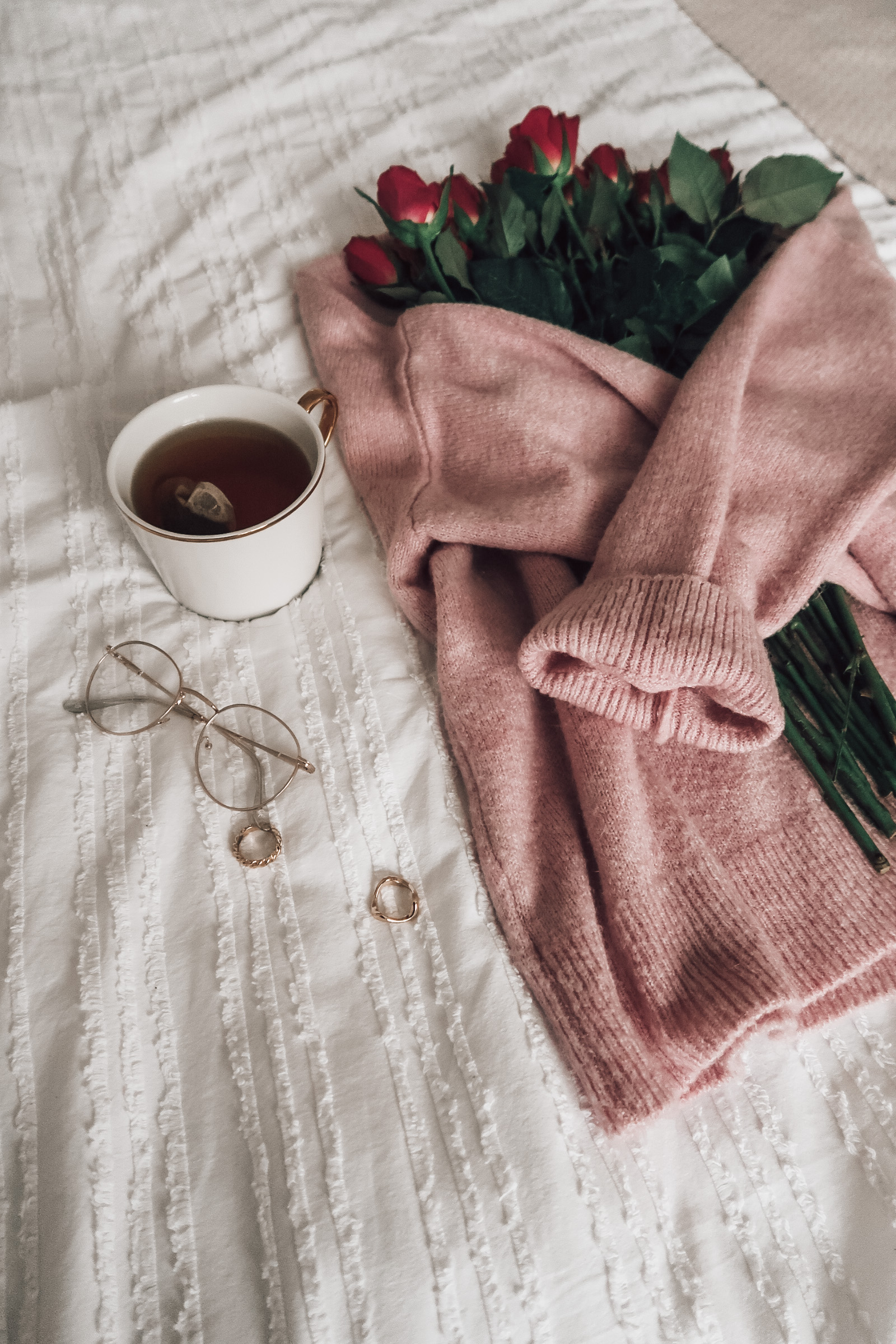 A light pink jumper wrapped around pink tulips with a white mug.