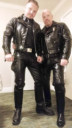 Two leather daddy lovers in full black leather gear posing for the camera