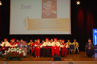 Na scenie w strojach reprezentacyjnych siedzą pracownicy Politechniki, za nimi na ekranie postać Profesora.