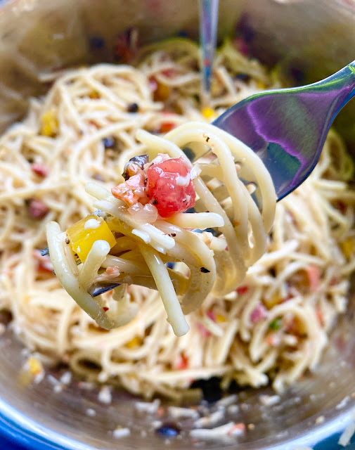 A fork spun with spaghetti salad with a bowl of it in the background.