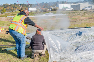 two people lifting a plastic sheet with steam coming out