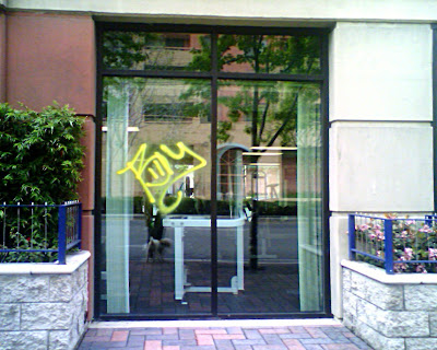 Two windows of an exercise room at 235 on Market Billy is spray painted in yellow spray paint on one of the windows.