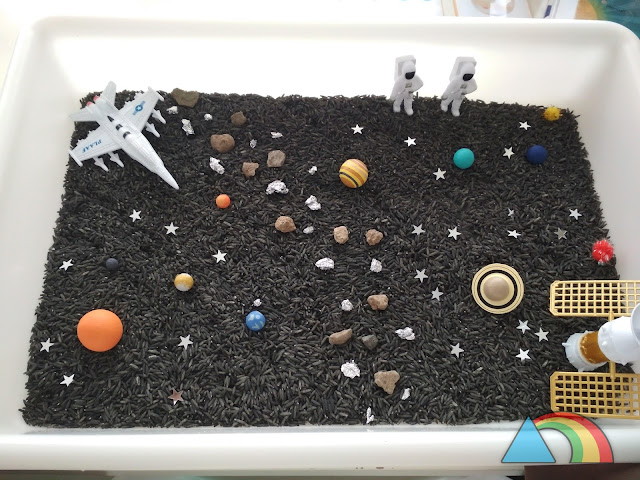 Bandeja con arroz teñido de negro, planetas del sistema solar en miniatura, piedras, confeti, naves y astronautas de juguete.