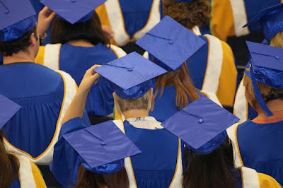 Crowd wearing graduation caps and gowns, viewed from behind