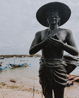 Estátua de pescador com barcos na água ao fundo