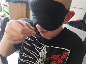 A in a spider man t shirt holding a spoon of mind sauce for testing wearing his black blindfold