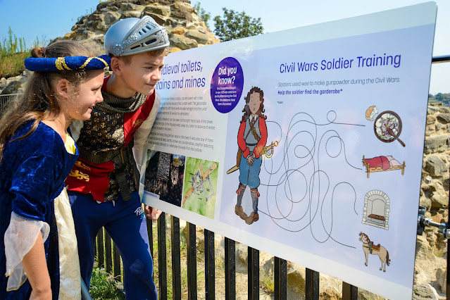 Two young visitors inspecting an information panel at Pontefract Castle. They are dressed up in medieval-style fancy dress.