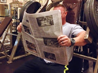 Bodybuilder reading newspaper on gym equipment