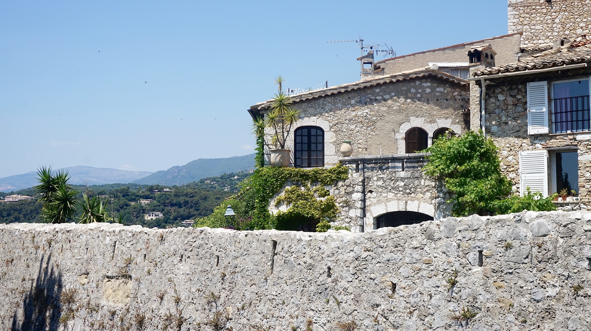 an old stone cottage behind a stone wall overlooking green trees and a blue sky