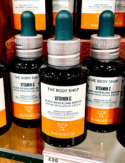 A close up of three small cylindrical dark black bottles with white pipette lids with a white lid that says vitamin c glow revealing serum with an orange strip at the tip with the the body shop all in black font on a bright background