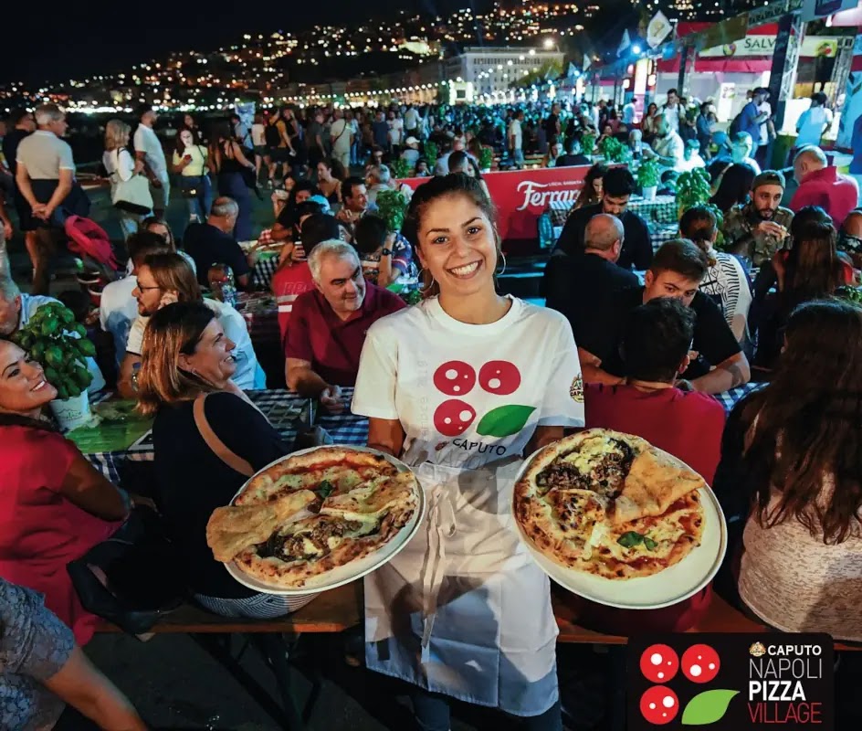 Una ragazza porta con due pizze al Napoli Pizza Village