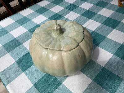 A ceramic pumpkin sitting on a green and white checkered table.