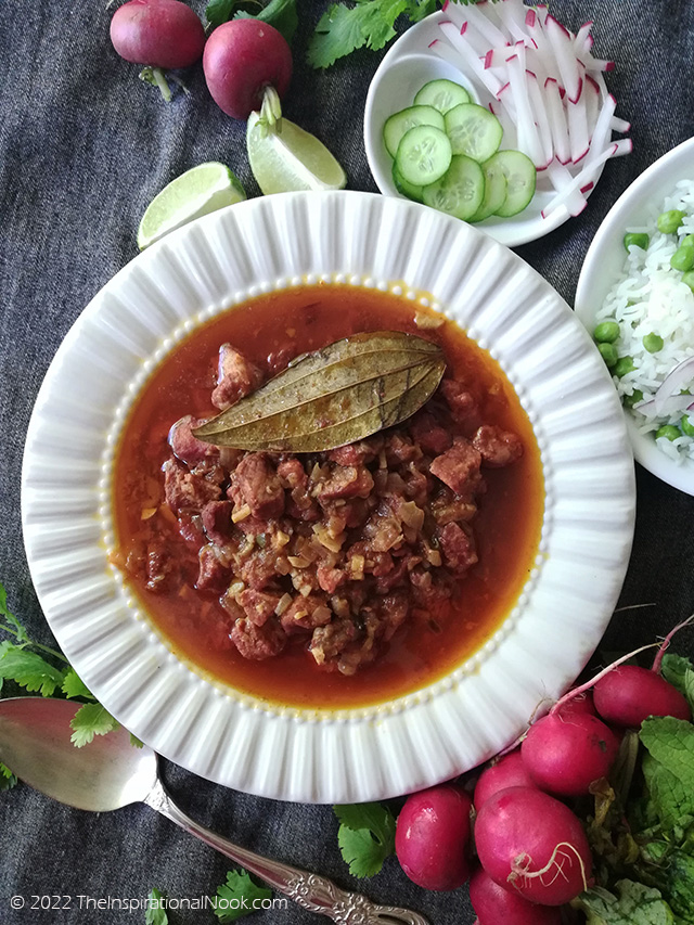 Pork bafat in a white bowl surrounded by red radishes, coriander leaves, peas, white rice and lime