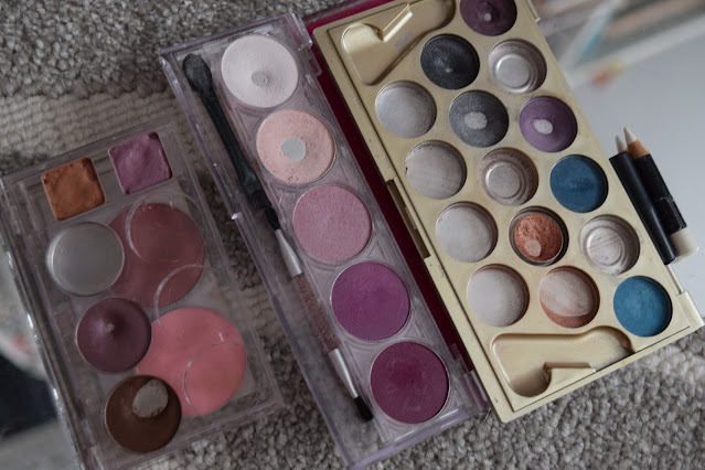 An eyeshadow palette with 11 pans in the centre and one with 4 to the left. Both palettes have a lot of visible use with 9 pans showing and 2 pans respectively. There is one more palette on the far right with 5 shades, two with pan showing.