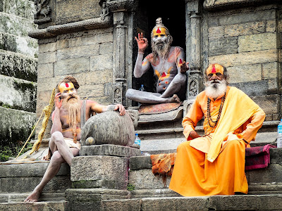 Two topless saints and another in orange sits at temple 