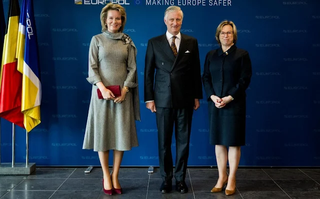 Queen Mathilde wears a black and white checked dress, with a wine-red cape coat by Natan. Diamond parrots brooch