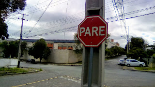 Fotografia de uma placa sinalizadora de trânsito encostada num poste de energia elétrica. Nela está escrito a palavra "pare" em letras maiúsculas.