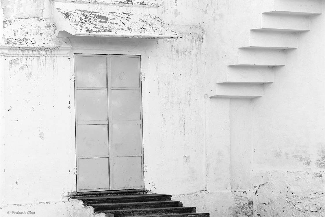 A Black and white Minimalist Photo of Steps leading to a closed door on the street right outside the Jharkhand Mahadev Temple in Vaishali Nagar Jaipur.